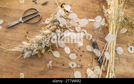 Arrangement floral séché sur une table en bois avec des ciseaux et des paquets de blé et de fleurs Banque D'Images