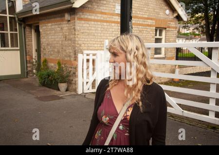 En attente d'aventure : une jeune femme au sourire captivant attend le train du patrimoine à la gare, jetant un regard franc au loin Banque D'Images