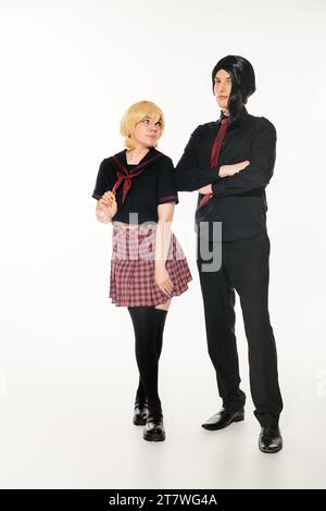 femme en perruque blonde regardant l'homme dans des vêtements noirs avec les bras pliés sur blanc, les étudiants de style anime Banque D'Images