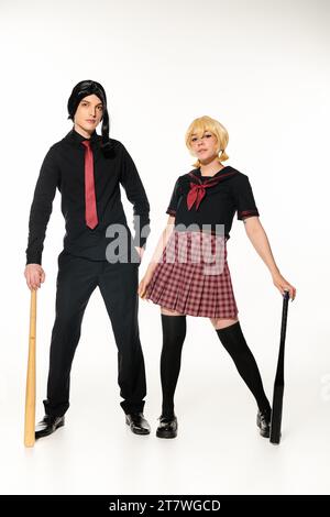 couple de cosplayers en uniforme scolaire et perruques avec battes de baseball sur blanc, pleine longueur Banque D'Images