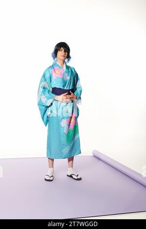 pleine longueur de jeune homme en kimono bleu et perruque sur tapis violet en studio blanc, concept cosplay Banque D'Images