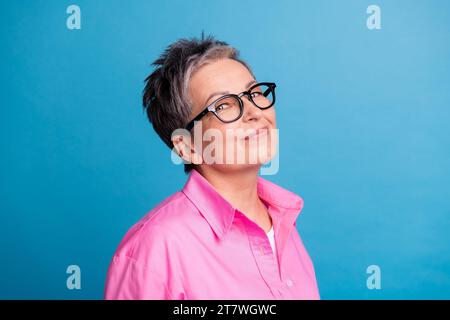 Photo de femme intelligente positive intelligente avec une chemise rose habillée de cheveux courts dans des lunettes regarder la caméra isolée sur fond de couleur bleue Banque D'Images