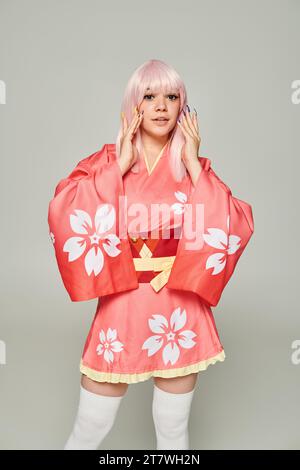 jeune femme blonde avec manucure colorée portant kimono rose et regardant la caméra sur gris Banque D'Images