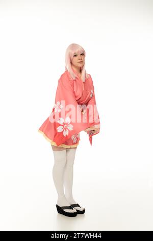 toute la longueur de jeune modèle avec les cheveux blonds posant en kimono rose et chaussettes de genou blanches sur blanc Banque D'Images