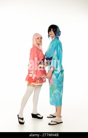 pleine longueur de jeunes cosplayers en kimonos colorés tenant les mains sur et regardant la caméra sur blanc Banque D'Images