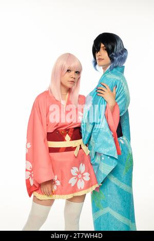 femme blonde de style anime embrassant le bras de l'homme en kimono et perruque sur blanc, concept de sous-culture cosplay Banque D'Images