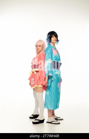 jeunes cosplayers en kimonos colorés et perruques debout dos à dos et tenant les mains sur le blanc Banque D'Images