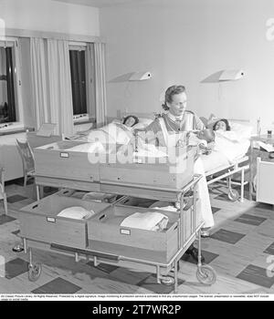 Intérieur de la salle pour les nouvelles mères à Södersjukhuset à Stockholm où une sage-femme tient un nouveau-né. Les nouveau-nés sont couchés dans des boîtes en bois sur un chariot. Les boîtes sont étiquetées avec des numéros et des noms. Sur la boîte dans laquelle la sage-femme mettra le bébé, il est indiqué 43 Lindberg, qui est une fille qui pesait 3650 grammes. Les nouvelles mères sont couchées dans des lits dans la chambre. Suède 1949. Kristoffersson réf AU33-1 Banque D'Images