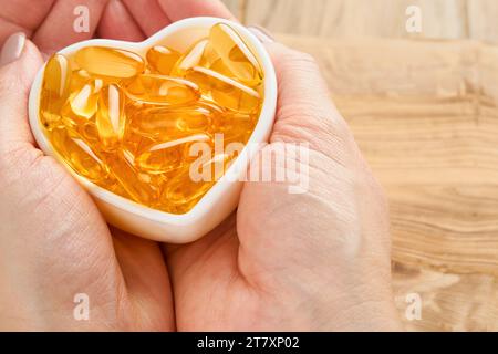 Femme ou médecin tient dans la main des capsules avec de la vitamine D, E ou des acides gras oméga 3,6,9 dans un bol en forme de coeur. Huile de poisson remplie d'huile de complément alimentaire. Naturel Banque D'Images