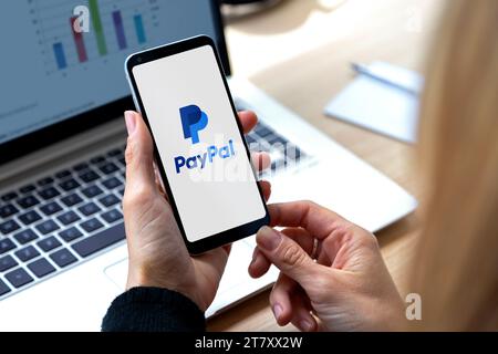 Application PayPal sur l'écran du smartphone. Femme devant un ordinateur portable avec un téléphone portable dans les mains. Logotype du système de paiement électronique. Rosario, Arg Banque D'Images