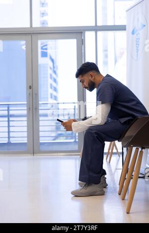 Médecin masculin biracial à l'aide du smartphone dans la salle d'attente de l'hôpital Banque D'Images