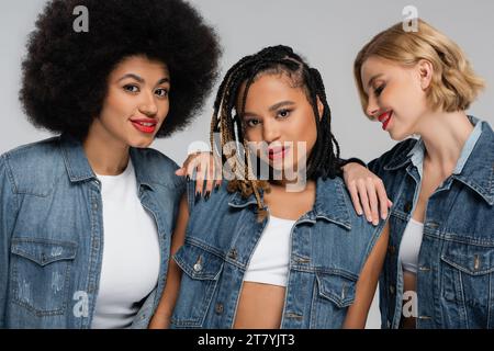 diverses et charmantes copines multiraciales en tenue de denim bleu posant sur la mode grise et moderne Banque D'Images