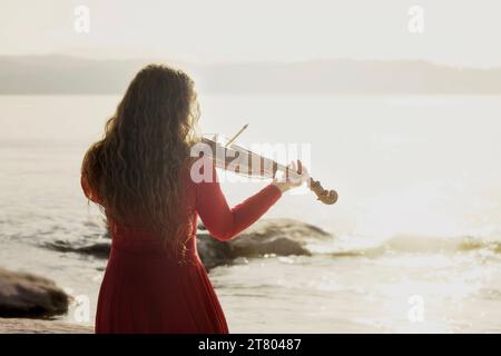 scène romantique d'une femme jouant du violon devant la mer Banque D'Images