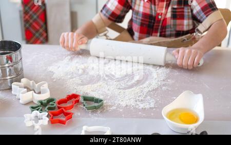 Fille apprenant à cuisiner, déroule la pâte avec un rouleau à pâtisserie, aide dans la cuisine blanche et des biscuits pour Noël et le nouvel an. Banque D'Images