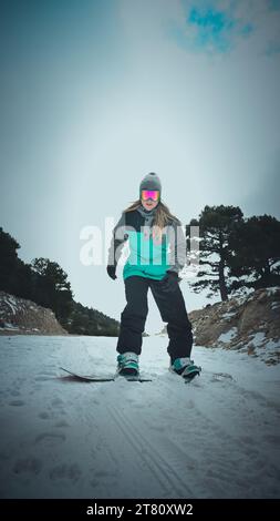 Une femme snowboardeuse en position prête au sommet d'une colline, alors qu'elle se prépare à faire une promenade palpitante sur les pentes enneigées Banque D'Images