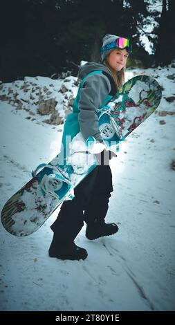 Un jeune souriant se tient sur une colline enneigée, tenant un snowboard dans sa main Banque D'Images
