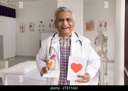 Joyeux vieux médecin cardiologue indien posant dans un cabinet hospitalier Banque D'Images