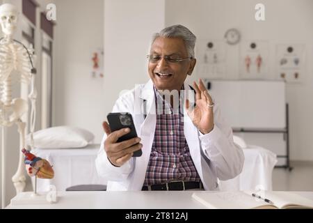 Joyeux homme médecin indien senior donnant consultation en ligne sur smartphone Banque D'Images