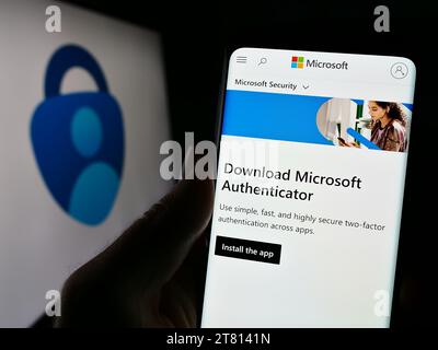 Personne tenant le téléphone portable avec la page Web de l'application d'authentification Microsoft Authenticator devant le logo de l'entreprise. Concentrez-vous sur le centre de l'écran du téléphone. Banque D'Images