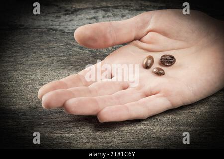 Thème du café. Trois grains de café se trouvent sur une feuille verte dans un gros plan de la main humaine. Banque D'Images