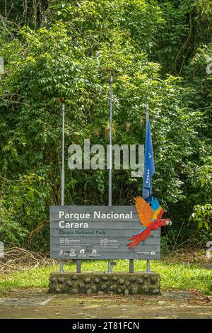 Costa Rica, Parque Nacional Carara - 22 juillet 2023 : en gros plan, panneau de bienvenue officiel blanc sur bois gris avec image d'aras écarlate et drapeau bleu. Vert Banque D'Images