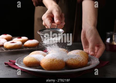 Femme saupoudrant le sucre en poudre sur de délicieux beignets Hanukkah sur la table grise, gros plan Banque D'Images