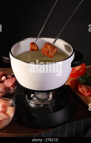 Tremper des morceaux de viande frite dans de l'huile dans un pot à fondue à la table en bois Banque D'Images