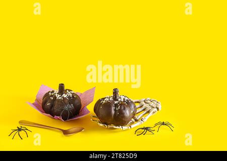 Délicieux gâteaux au chocolat, main squelette et cuillère pour la célébration d'Halloween sur fond jaune Banque D'Images