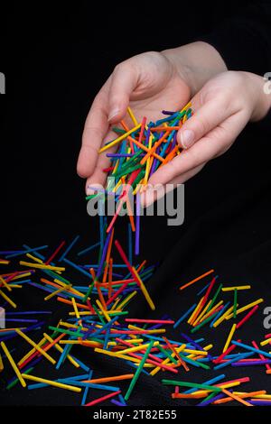 Main laissant des bâtons en bois de couleur tomber sur fond noir Banque D'Images