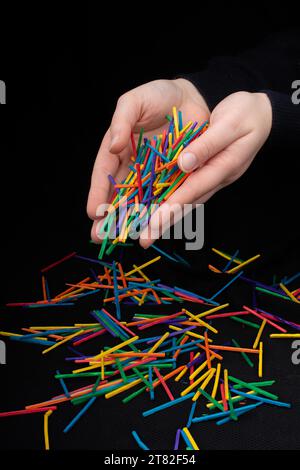 Main laissant des bâtons en bois de couleur tomber sur fond noir Banque D'Images