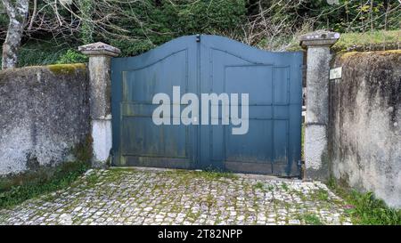 Une vieille clôture en pierre garnie de plâtre et envahie de mousse entre deux piliers de béton, une porte en fer gris Banque D'Images
