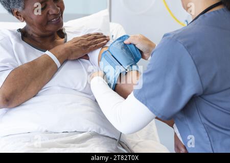 Divers médecin féminin testant la pression artérielle de la patiente âgée dans la chambre d'hôpital Banque D'Images