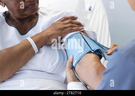 Divers médecin féminin testant la pression artérielle de la patiente âgée dans la chambre d'hôpital Banque D'Images