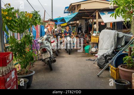 Les gens sur un scooter sur un sentier à côté d'un khlong ou canal avec des bâtiments résidentiels dans le district de Pattaya Chonburi Thaïlande Asie Banque D'Images