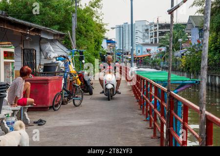 Les gens sur un scooter sur un sentier à côté d'un khlong ou canal avec des bâtiments résidentiels dans le district de Pattaya Chonburi Thaïlande Asie Banque D'Images