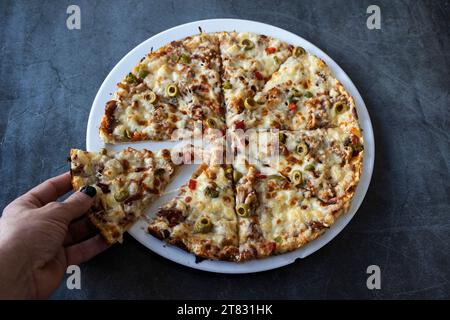Les mains de l'homme tenant la tranche de pizza kebab sur la table de restaurant vue de dessus plat Banque D'Images