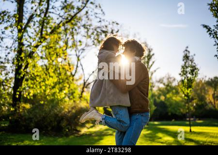 Portrait d'heureux couple amoureux dans le parc au coucher du soleil. L'homme tient sa femme entre les mains. Banque D'Images