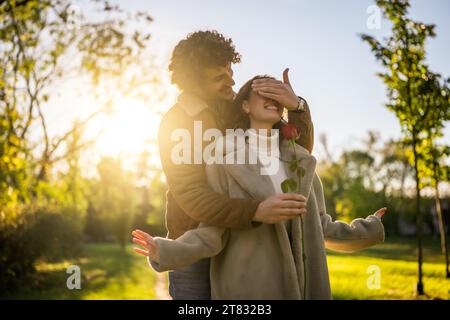 Portrait d'heureux couple amoureux dans le parc au coucher du soleil. L'homme donne de la rose à sa femme. Banque D'Images