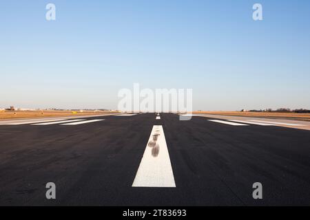 Niveau de surface de la longue piste de l'aéroport avec marquage directionnel sur ciel dégagé. Banque D'Images