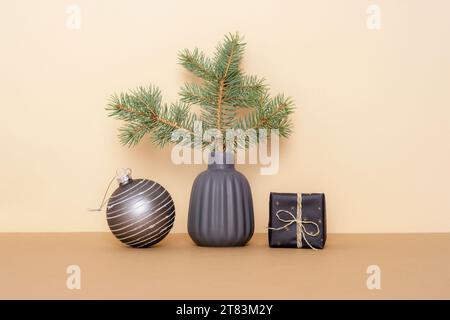 Branche d'épicéa dans un vase en céramique, boîte cadeau et boule de Noël sur table beige. Concept de Noël minimal. Banque D'Images