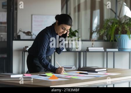 Sérieuse et occupée jeune femme d'affaires indienne travaillant avec des papiers collants Banque D'Images