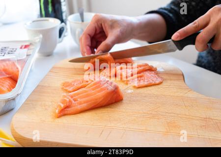 Chef masculin à l'aide d'un couteau coupant le filet de saumon cru sur la planche à découper dans la cuisine. Cuisson du sashimi de saumon Banque D'Images