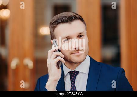 Homme professionnel en costume bleu sur le téléphone, regard confiant, portes en bois Banque D'Images