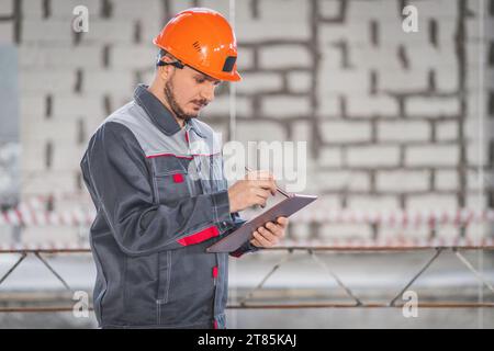 Travailleur caucasien sur un chantier de construction utilise une tablette numérique dans ses activités professionnelles, espace de copie Banque D'Images