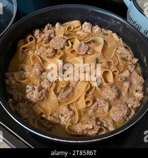 Une poêle en acier inoxydable remplie de boulettes de viande suédoises fraîchement cuites et de pâtes larges dans une poêle sur la cuisinière Banque D'Images