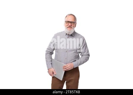 homme d'affaires mature aux cheveux gris réussi avec une barbe et une moustache dans une chemise et un pantalon tient un ordinateur portable Banque D'Images