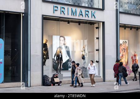 Les acheteurs et les visiteurs à l'extérieur passent devant un homme assis sur le trottoir demandant de l'argent pour aider à payer une auberge de jeunesse de la marque de vêtements Primark sur Oxford Street le 13 novembre 2023 à Londres, Royaume-Uni. Oxford Street est un important centre de vente au détail dans le West End de la capitale et est la rue commerçante la plus achalandée d'Europe avec environ un demi-million de visiteurs quotidiens dans ses quelque 300 boutiques, dont la majorité sont des magasins de mode et de vêtements de grande rue. Banque D'Images