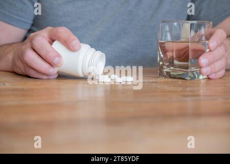 Personne avec des pilules et un verre d'eau dans la cuisine. Banque D'Images