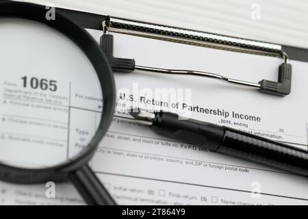 IRS Form 1065 US Return of Partnership Income blanc sur la tablette A4 repose sur la table de bureau avec stylo et loupe en gros plan Banque D'Images