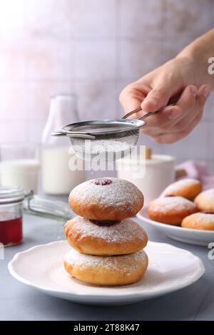 Femme saupoudrant le sucre en poudre sur de délicieux beignets Hanukkah sur la table gris clair, gros plan Banque D'Images